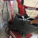 A mechanic in black gloves using a red tire changer machine to mount a tire onto a Volkswagen alloy rim.