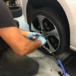 A technician using a pneumatic impact wrench to tighten lug nuts on a car wheel with a black and silver rim.